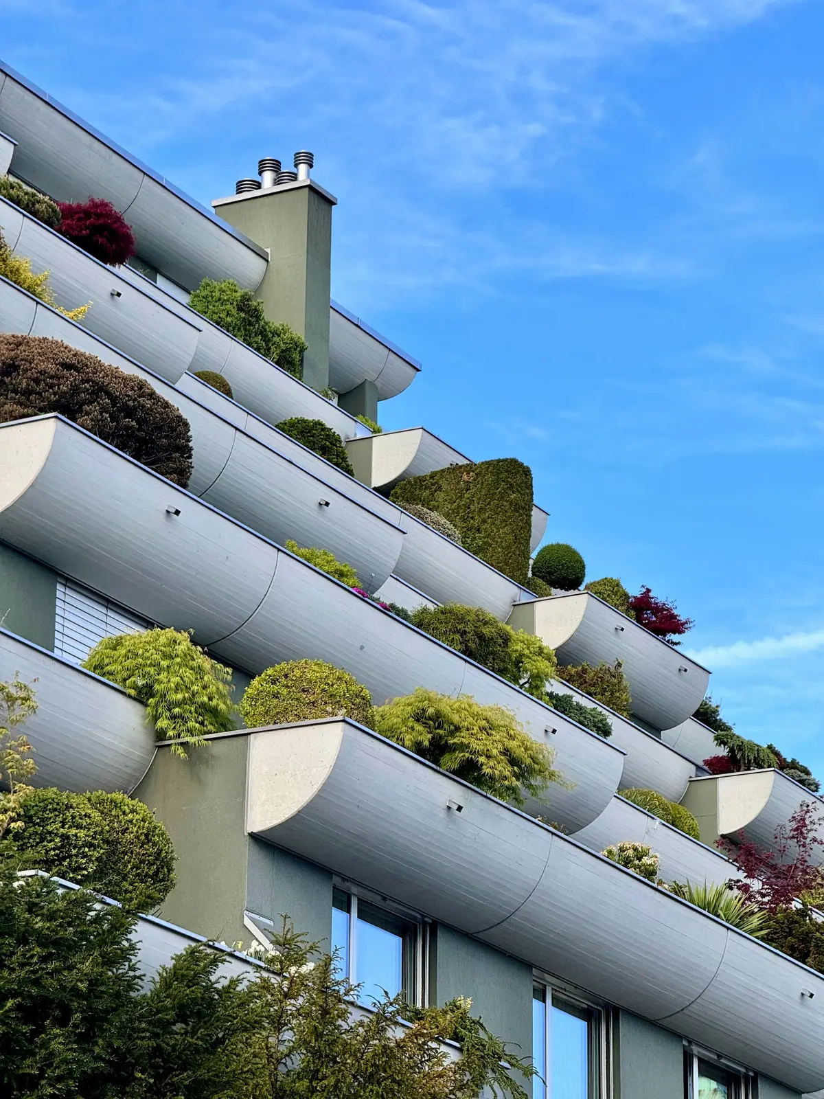 Fachada de un edificio residencial urbano con terrazas ajardinadas y arbustos en cada planta